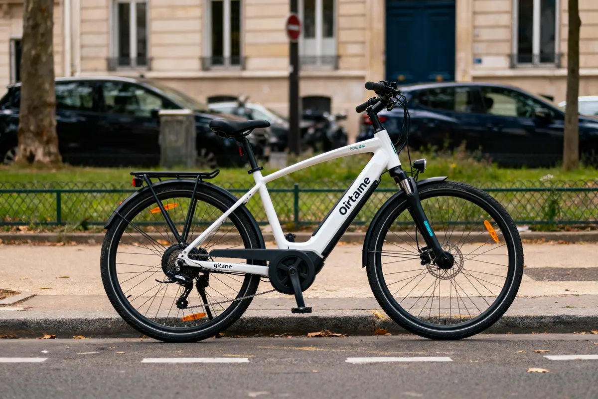 Vélo électrique blanc stationné sur le trottoir, au bord de la route, devant un immeuble urbain.