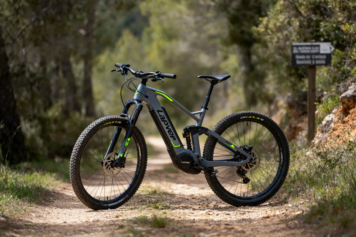 Vélo électrique Lapver sur un chemin boisé, signalisation en arrière-plan, ambiance extérieure naturelle.