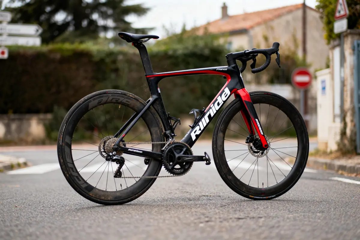 Vélo de route noir et rouge, stationné sur une route urbaine, cercles de roue en carbone.