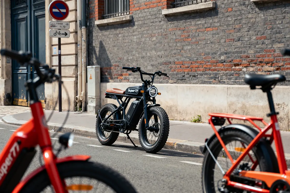 Vélos électriques garés dans la rue près d'un mur en briques, panneau interdit stationner visible.
