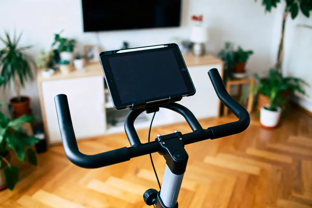 Vélo d'appartement avec tablette sur guidon, intérieur moderne avec plantes.